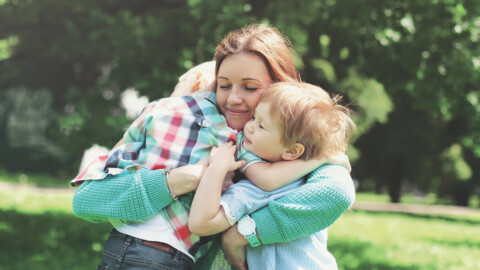 Happy smiling mother is embracing children at summer day